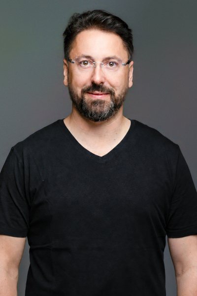 Niko Martzy im schwarzen T-Shirt vor grauem Hintergrund, freundlich lächelnd